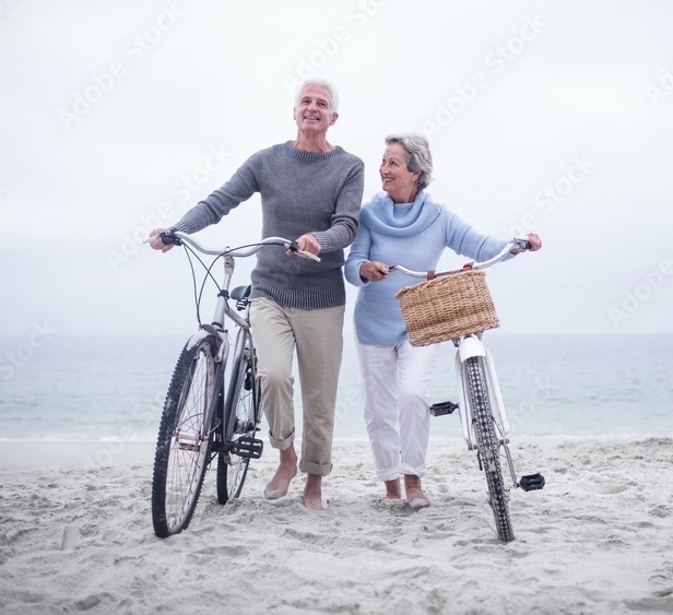 Older couple walking bicycles on a beach
